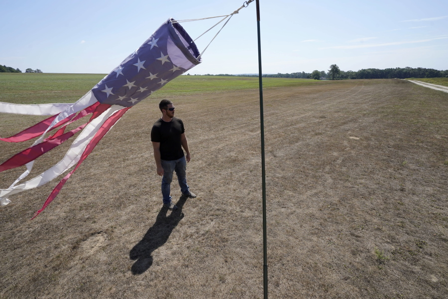 Hay farmer Milan Adams stands in a dry hay field near a wind sock, left, in Exeter, R.I., Tuesday, Aug. 9, 2022. Adams said in prior years it rained in the spring. This year, he said, the dryness started in March, and April was so dry he was nervous about his first cut of hay.
