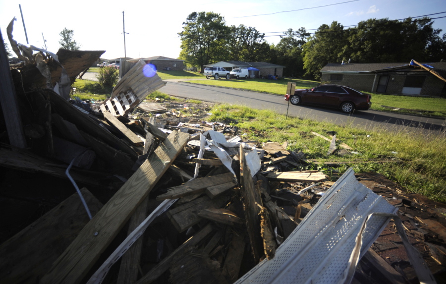 A car passes between a pile of storm debris and a damaged home, Wednesday, July 27, 2022, nearly four months after a small tornado shattered Branch Heights, a rural housing community in Eutaw, Ala. Some worry the continuing recovery shows how hard it may be to get over a big storm as the heart of hurricane season approaches the U.S. Gulf Coast.