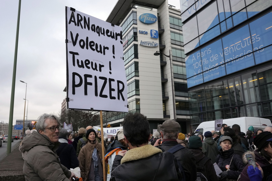 FILE - A demonstrator holds a placard reading "Scammer, thief, killer, Pfizer" during a protest against the vaccine pass and vaccinations to protect against COVID-19 in front of the Pfizer headquarters, in Paris, on Jan. 29, 2022. An anti-vaccine group that has harassed doctors and public officials in Italy and France is still active on platforms like Facebook despite efforts to rein in their abuse and misinformation. The organization, known as V--V, bombards its victims with dozens, hundreds or even thousands of abusive posts.
