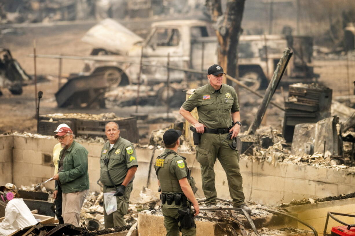 Sheriff's Deputy Johnson stands at a burned home as search and rescue workers recover the remains of a McKinney Fire victim on Monday, Aug. 1, 2022, in Klamath National Forest, Calif.