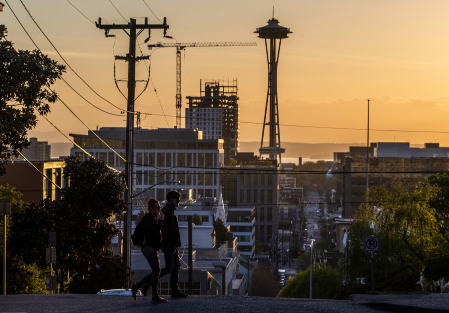 Two people walk along Bellevue Avenue while the sun sets in Capitol Hill on Thursday, April 22, 2021, in Seattle.