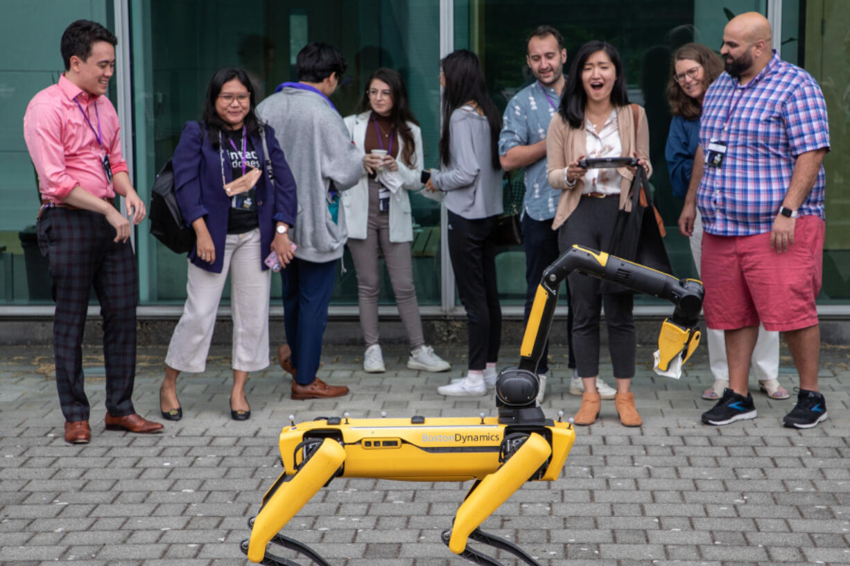 Mia Qu, third from right, a second-year student at the University of Washington Law School, gasps in delight after making Spot, an AI robot created by Boston Dynamics, pick up a cup during the We Robot 2022 conference at UW on Sept. 15, 2022, in Seattle. The robot is intended to easily navigate and gather data in rough terrain.