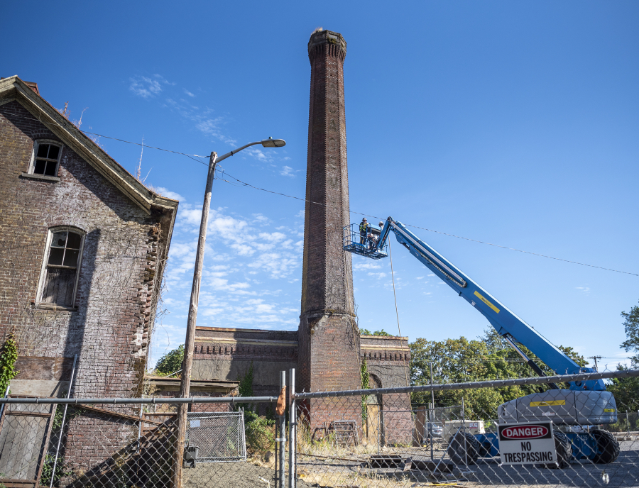 Workers begin the brick-by-brick demolition of Providence Academy's smokestack on Wednesday. The iconic structure, built in 1910 along with a boiler room that warmed neighboring Academy buildings, was deemed too expensive to restore and several preservation efforts over the years were unsuccessful.