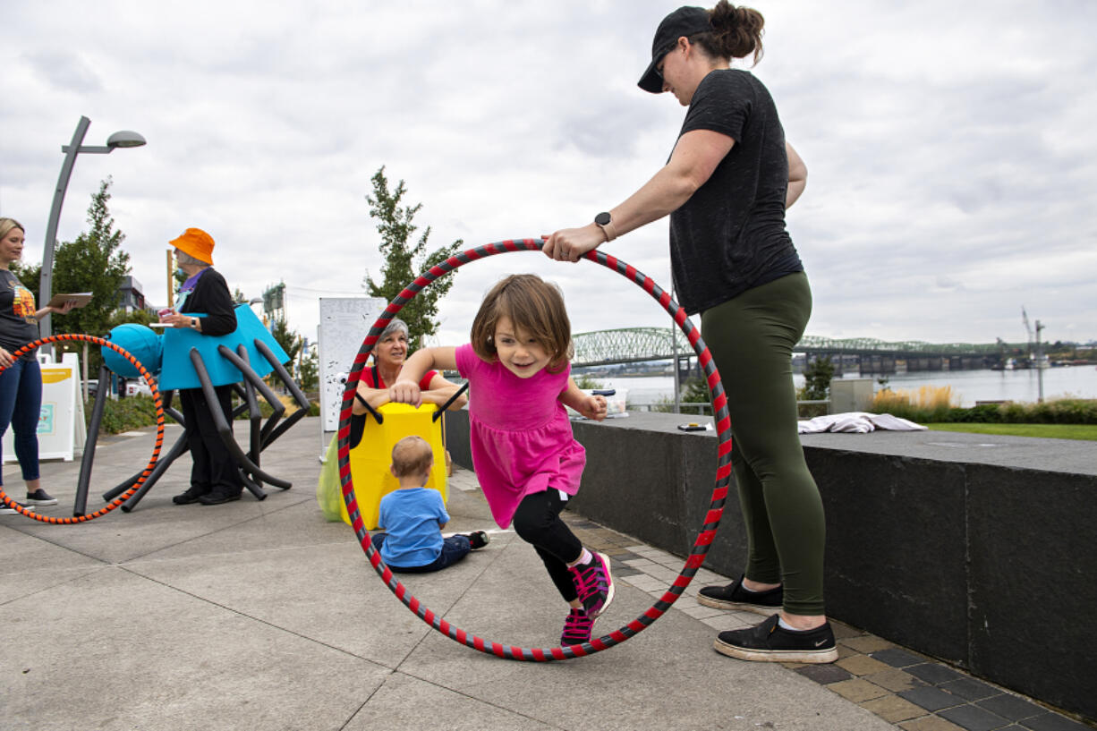 Katie Gregg, 2, of Vancouver leaps through a hula hoop held by her mom, Tiffany, as they stop by to explore toys from the Columbia Play Project at The Waterfront Vancouver on Thursday. The playtime was part of the annual Give More 24! day of fundraising.