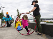 Katie Gregg, 2, of Vancouver leaps through a hula hoop held by her mom, Tiffany, as they stop by to explore toys from the Columbia Play Project at The Waterfront Vancouver on Thursday. The playtime was part of the annual Give More 24! day of fundraising.