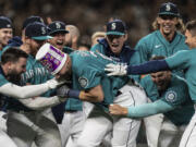 Seattle Mariners including Jesse Winker, left; Ty France, third from right; Logan Gilbert, second from right; and Adam Frazier, right celebrate a home run by Cal Raleigh in ninth inning of a baseball game against the Oakland Athletics, Friday, Sept. 30, 2022, in Seattle. The Mariners won 2-1 to clinch a spot in the playoffs.