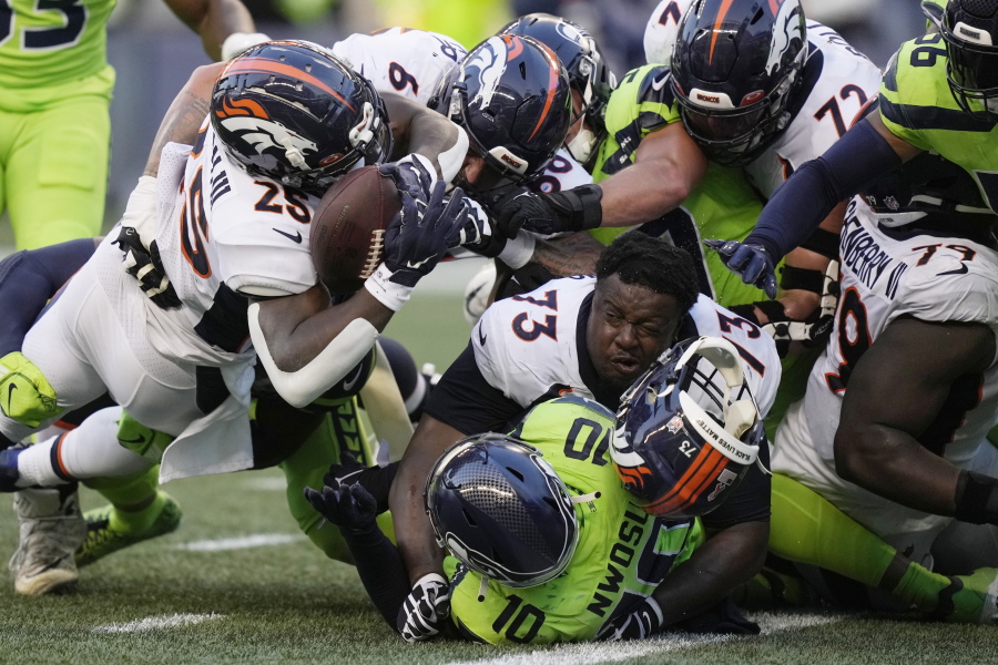 Denver Broncos running back Melvin Gordon III, upper left, fumbles the ball as Broncos offensive tackle Cameron Fleming (73) loses his helmet during the second half of an NFL football game against the Seattle Seahawks, Monday, Sept. 12, 2022, in Seattle.