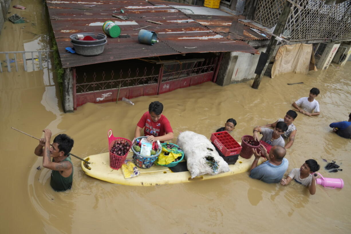 Residents give away onions and other foods along a flooded road due to Typhoon Noru in San Miguel town, Bulacan province, Philippines, Monday, Sept. 26, 2022. Typhoon Noru blew out of the northern Philippines on Monday, leaving some people dead, causing floods and power outages and forcing officials to suspend classes and government work in the capital and outlying provinces.