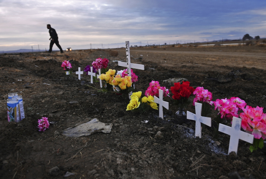 FILE - A row of crosses form a memorial along Highway 33 as police officers survey the scene a day after a crash killed nine people south of Coalinga, Calif., Saturday, Jan. 2, 2021. Investigators said the driver of an SUV involved in the crash was drunk and didn't have a license. The National Transportation Safety Board will use a final report on the crash to launch an effort to lobby for regulations requiring alcohol breath testing devices on all new vehicles.