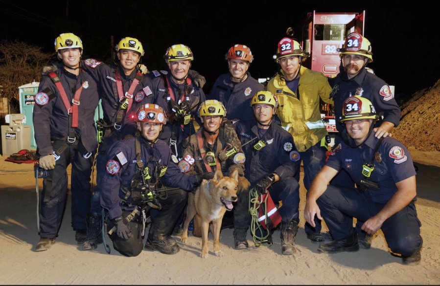 This image provided by the Pasadena Fire Department showing firefighters pose with a Cesar a blind dog that was rescued from a hold in Pasadena, Calif. on Tuesday, Sept. 20, 2022. Firefighters have rescued a 13-year-old blind dog that fell into a hole at a California construction site. The dog, named Cesar, lives next to the site in Pasadena with his owner. He apparently wandered onto the site, said Cesar's owner Mary, who declined to give her last name.
