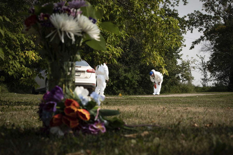 Investigators examine the crime scene near a memorial of flowers outside the home of Wes Petterson in Weldon, Saskatchewan, Monday, Sept. 5, 2022. Petterson, 77, was killed in a series of stabbings in the area on Sunday.