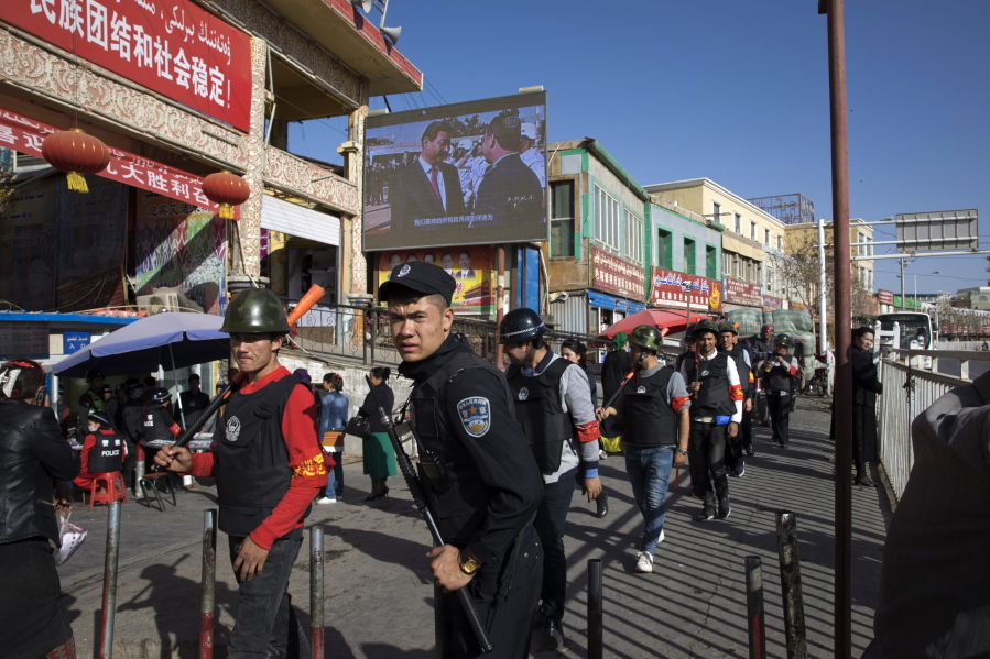 FILE - Armed civilians patrol the area outside the Hotan Bazaar where a screen shows Chinese President Xi Jinping in Hotan in western China's Xinjiang region, Nov. 3, 2017. China's discriminatory detention of Uyghurs and other mostly Muslim ethnic groups in the western region of Xinjiang may constitute crimes against humanity, the U.N. human rights office said in a long-awaited report Wednesday, Aug. 31, 2022, which cited "serious" rights violations and patterns of torture in recent years.