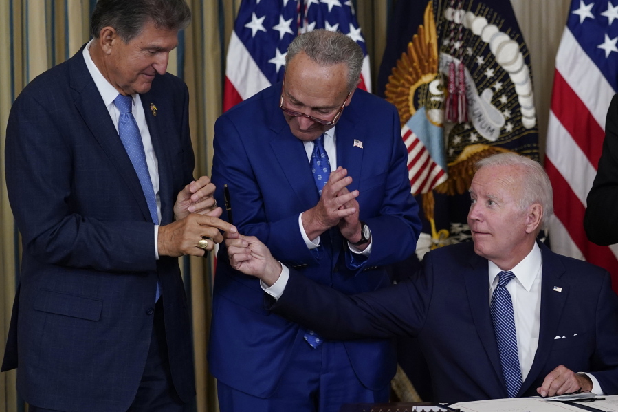 FILE - President Joe Biden hands the pen he used to sign the Democrats' landmark climate change and health care bill to Sen. Joe Manchin, D-W.Va., as Senate Majority Leader Chuck Schumer of N.Y., watches in the State Dining Room of the White House in Washington, Aug. 16, 2022. Manchin made a deal with Democratic leaders as part of his vote pushing the party's highest legislative priority across the finish line last month. Now, he's ready to collect. But many environmental advocacy groups and lawmakers are balking.