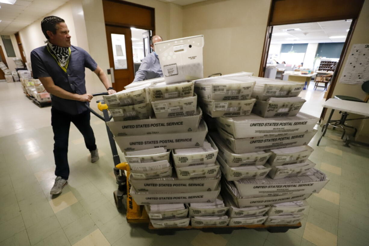 FILE - Chet Harhut, deputy manager, of the Allegheny County Division of Elections, wheels a dolly loaded with mail-in ballots, at the division of elections offices in downtown Pittsburgh, May 27, 2020. State laws in the crucial battleground states of Pennsylvania, Michigan and Wisconsin force most mail-in ballots to be processed and counted after Election Day, sometimes stretching the process by a week or more. That lag time in getting results opens the door to lies and misinformation that can sow distrust about the eventual outcome in close races. (AP Photo/Gene J.