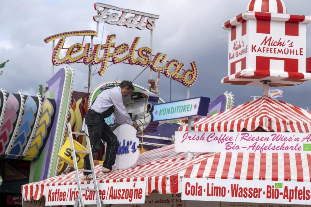 A man mounts a light advertisement on a booth on the Oktoberfest grounds in Munich, Germany, Thursday, Sept. 15, 2022. The Oktoberfest is on tap again in Germany after a two-year pandemic interruption. The beer will be just as cold and the pork knuckle just as juicy. But brewers and visitors are under pressure from inflation in ways they could hardly imagine in 2019.