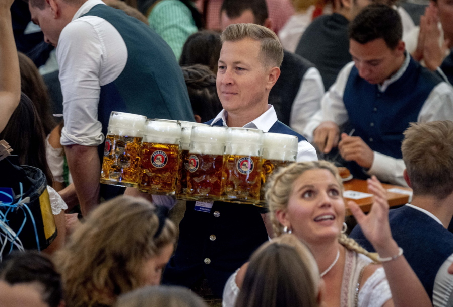 A waiter carries beer in one of the beer tents on the opening day of the 187th Oktoberfest beer festival in Munich, Germany, Saturday, Sept. 17, 2022. Oktoberfest is back in Germany after two years of pandemic cancellations, the same bicep-challenging beer mugs, fat-dripping pork knuckles, pretzels the size of dinner plates, men in leather shorts and women in cleavage-baring traditional dresses.