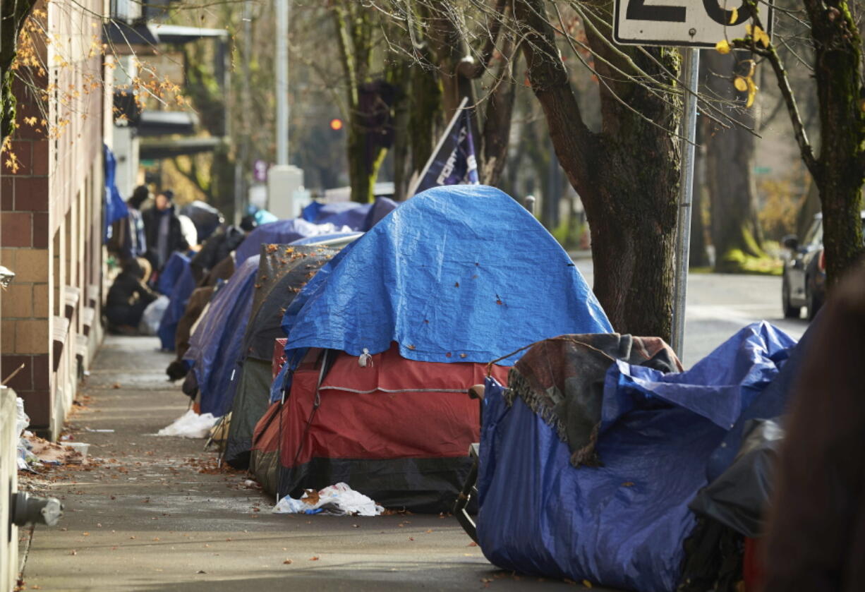 FILE - Tents line the sidewalk on SW Clay St in Portland, Ore., on Dec. 9, 2020. People with disabilities in Portland have filed a class action lawsuit in federal court, Thursday, Sept. 8, 2022, claiming the city has failed to keep sidewalks accessible by allowing homeless tents and encampments to block sidewalks.