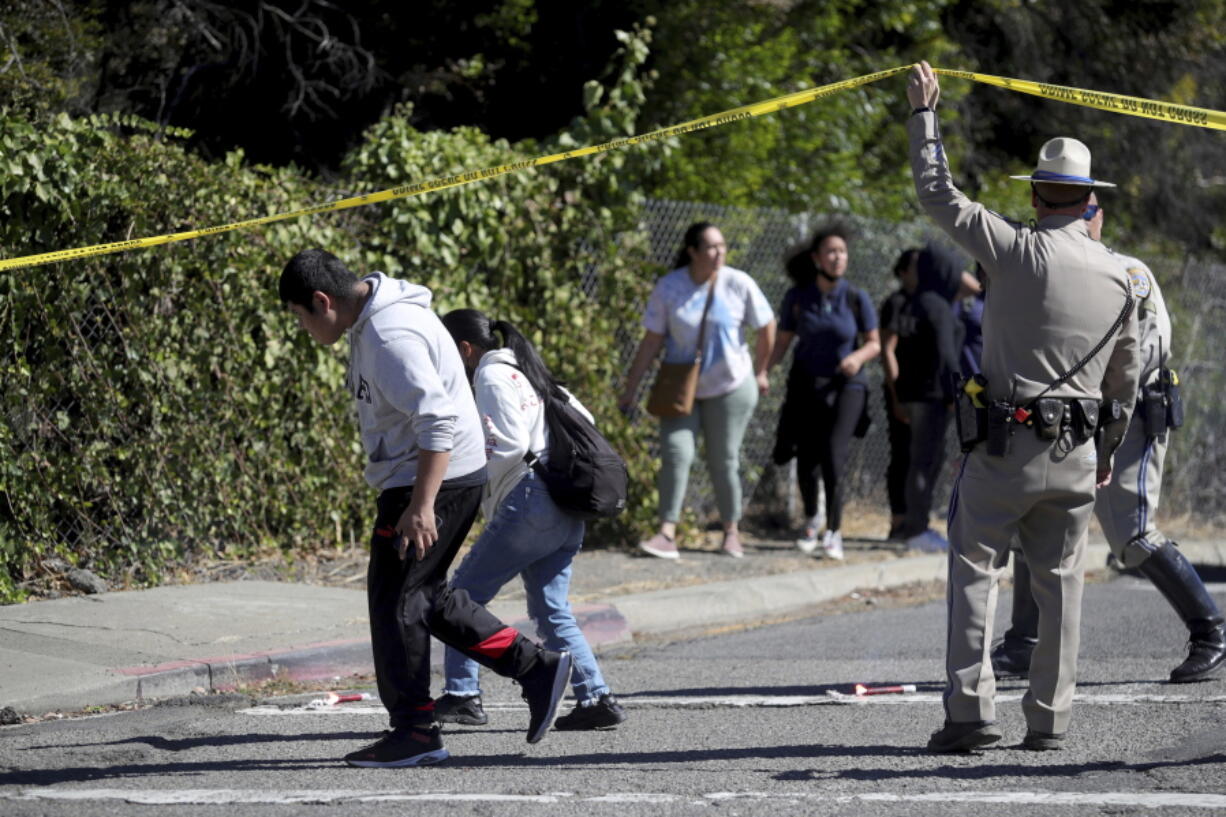 A California Highway Patrol officer lifts police tape to let parents and students leave a cordoned off area on Fountain Street following a shooting at a school campus in Oakland, Calif., on Wednesday, Sept. 28, 2022.
