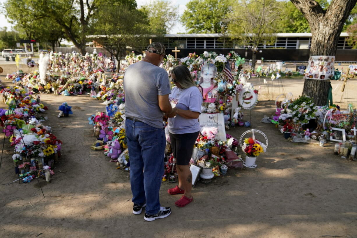 Pastor Wayne Traverse, from Port St.Lucie, Fla., left, prays with a woman at a make-shift memorial honoring the school shooting victims at Robb Elementary, Tuesday, July 12, 2022, in Uvalde, Texas.   Students who survived the May 24 shooting at an elementary school in Uvalde, Texas are spending the summer grappling with post-traumatic stress disorder. Meanwhile, parents find themselves unable to help them, worried the tragedy at Robb Elementary struck a largely Hispanic town as Latinos continue to face disparities to access mental health care.