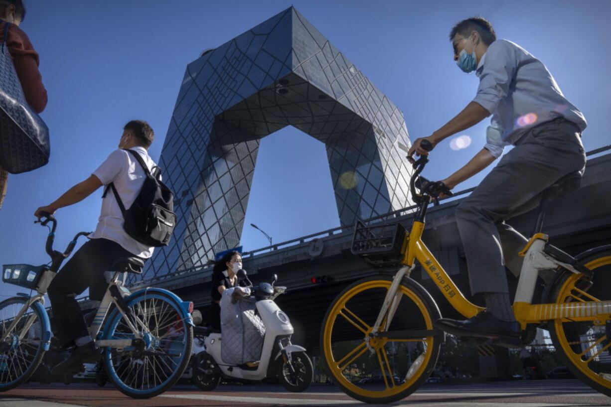 Commuters wearing face masks ride bicycles near the China Central Television (CCTV) building in the central business district in Beijing, Thursday, Sept. 1, 2022.