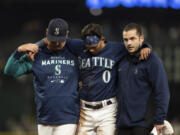 Seattle Mariners' Sam Haggerty, center, is helped off the field by training personnel manager Scott Servais, left, while stealing second base during the ninth inning of a baseball game against the Detroit Tigers, Monday, Oct. 3, 2022, in Seattle. The Tigers won 4-3.