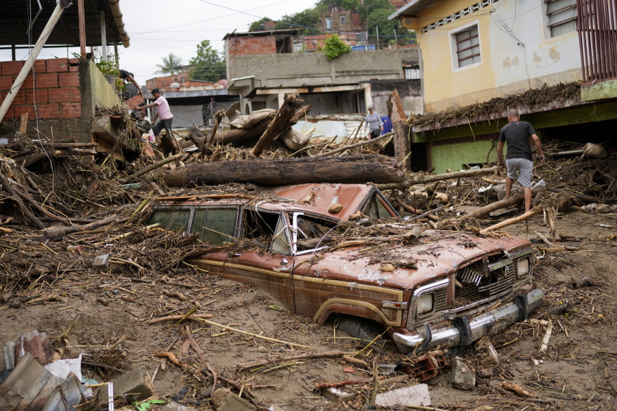 Residents walk through the debris left by flooding caused by a river that overflowed after days of intense rain in Las Tejerias, Venezuela, Sunday, Oct. 9, 2022.