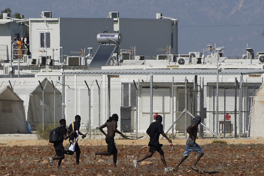 Migrants, holding what appear to be like weapons, flee the camp near the village of Kokkinotrimithia on the outskirts of the capital Nicosia, Cyprus, Friday, Oct. 28, 2022. Tensions inside the often overcrowded camp occasionally boil over into fighting as Cyprus continues to deal with large numbers of arriving migrants.