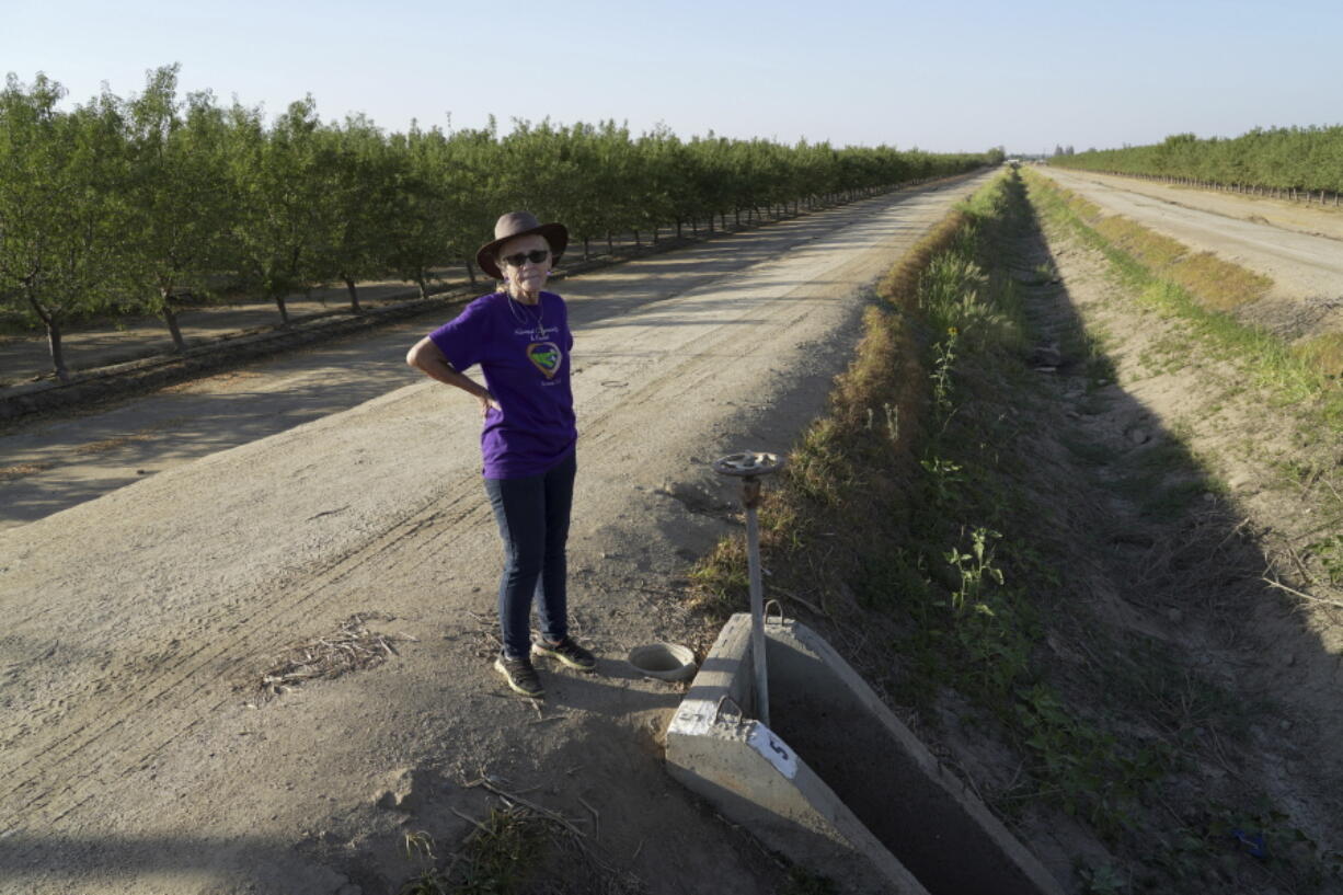 Elaine Moore stands next to a dry irrigation canal and almond orchard near her property, where two wells have gone dry this summer in Chowchilla, Calif., Sept. 14, 2022. Amid a megadrought plaguing the American West, more rural communities are losing access to groundwater as heavy pumping depletes underground aquifers that aren't being replenished by rain and snow.