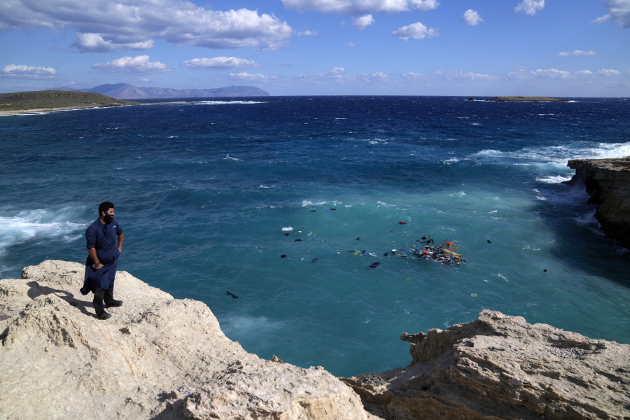 A local resident stands on a cliff as bodies of migrants are seen next floating debris after a sailboat carrying migrants smashed into rocks and sank off the island of Kythira, southern Greece, Thursday, Oct. 6, 2022. Residents of a Greek island pulled shipwrecked migrants to safety up steep cliffs in dramatic rescues after two boats sank in Greek waters, leaving at least 21 people dead and many still missing.