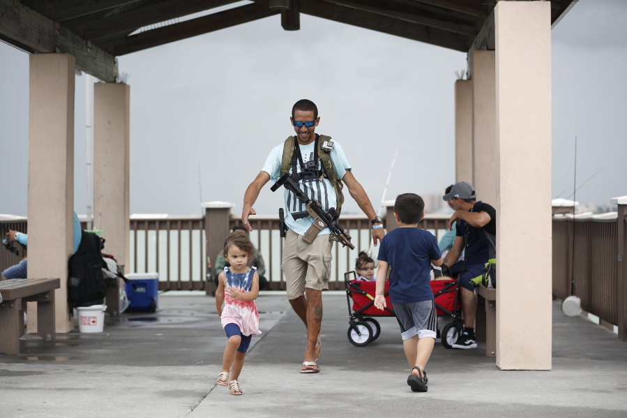 FILE - Michael Taylor, also known as "The Armed Fisherman", walks along Pier 60 in Clearwater Beach, Fla., with his 2-year-old daughter Ocean and his assault rifle and fishing gear, on July 3, 2021. Advocates say permitless carry makes people safer. Opponents say it makes it more dangerous for ordinary people, and for police officers.