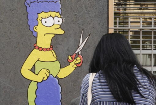 A woman takes pictures of a mural called "The Cut" by street artist aleXsandro Palombo depicting Marge Simpson, a character of the animated television series "The Simpsons" cutting her iconic hair, in front of the Consulate of Iran, in Milan, Italy, Wednesday, Oct. 5, 2022. Thousands of Iranians have taken to the streets over the last two weeks to protest the death of Mahsa Amini, a 22-year-old woman who had been detained by Iran's morality police in the capital of Tehran for allegedly not adhering to Iran's strict Islamic dress code.