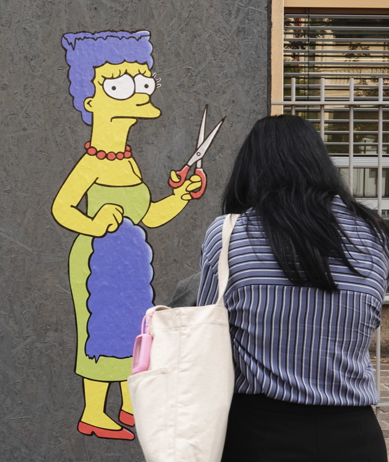 A woman takes pictures of a mural called "The Cut" by street artist aleXsandro Palombo depicting Marge Simpson, a character of the animated television series "The Simpsons" cutting her iconic hair, in front of the Consulate of Iran, in Milan, Italy, Wednesday, Oct. 5, 2022. Thousands of Iranians have taken to the streets over the last two weeks to protest the death of Mahsa Amini, a 22-year-old woman who had been detained by Iran's morality police in the capital of Tehran for allegedly not adhering to Iran's strict Islamic dress code.