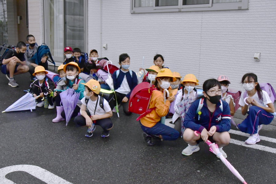 Elementary school students find shelter near a building on their way to school soon after a report of North Korea's missile launch, in Misawa, Aomori prefecture, northern Japan Tuesday, Oct. 4, 2022. North Korea on Tuesday fired an intermediate-range ballistic missile over Japan for the first time in five years, forcing Japan to issue evacuation notices and suspend trains during the flight of the weapon that is capable of reaching the U.S. territory of Guam.