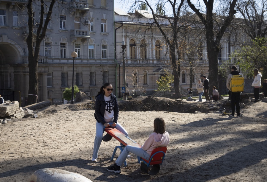 A mother and daughter play in a playground near a huge crater left by a Russian rocket a week ago, in central Kyiv, Ukraine, Sunday, Oct. 16, 2022. Ukrainians' resilience in the nearly 8-month-old war continues to be unwavering, despite an uptick in attacks that are seen as Russian President Vladimir Putin's vengeful response to an explosion that damaged a Moscow-built bridge to the Kremlin-annexed Crimean Peninsula on Oct. 8.