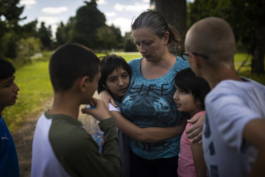 Olga Lopatkina embraces her adopted children in a park in Loue, western France, Saturday, July 2, 2022. After two months of negotiation and an initial objection from a senior Russian official, DPR authorities finally agreed to allow a volunteer with power of attorney from Lopatkina to collect her children who were evacuated from Mariupol. An Associated Press investigation has found that Russia's strategy to take Ukrainian orphans and bring them up as Russian is well underway.