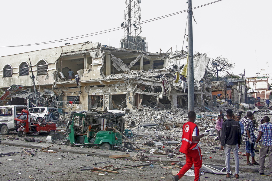 People observe a destroyed building and vehicles at the scene of a two car bombs attack in Mogadishu, Somalia, Saturday Oct. 29, 2022. Two car bombs exploded Saturday at a busy junction in Somalia's capital near key government offices, leaving "scores of civilian casualties," police told state media.