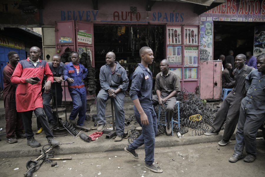 Workers gather as they wait for customers outside a secondhand car parts shop in the industrial area of the capital Nairobi, Kenya, Friday, Oct. 7, 2022. In a gritty neighborhood of Nairobi known for fixing cars and selling auto parts, businesses are struggling and customers are unhappy.