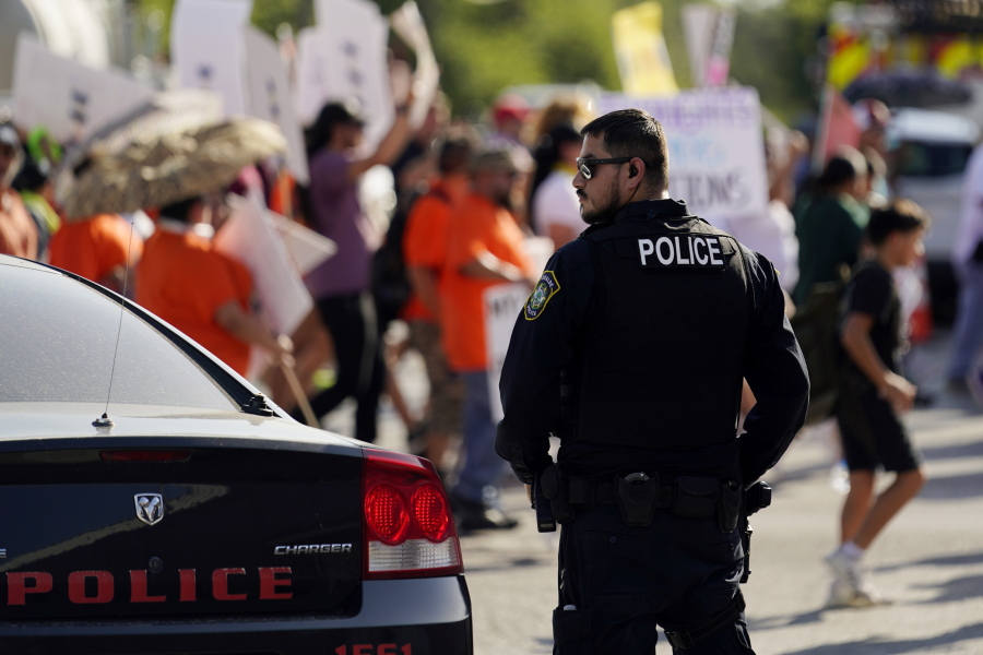 FILE - A Uvalde police officer watches as family and friends of those killed and injured in the school shootings at Robb Elementary take part in a protest march and rally, Sunday, July 10, 2022, in Uvalde, Texas.   Four months after the Robb Elementary School shooting, the Uvalde school district on Friday, Oct.