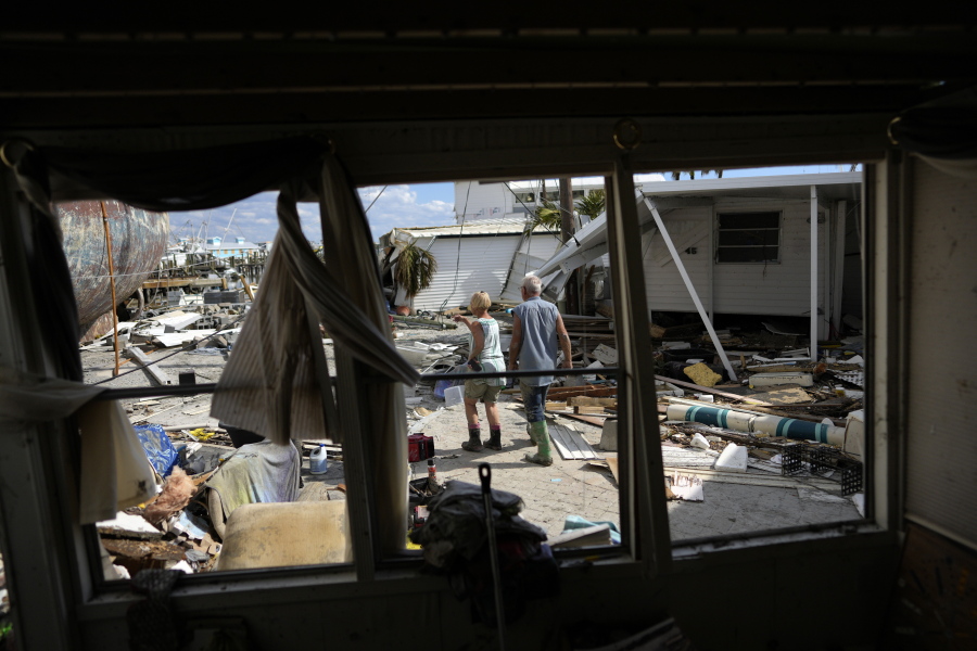 Snowbirds Bruce and Kathy Hickey, both 70, are seen through the windows of a trailer that had been waterfront, as they look at the wreckage of the trailer park where they had a winter home, originally purchased by Kathy's mother in 1979, on San Carlos Island, Fort Myers Beach, Fla., Wednesday, Oct. 5, 2022, one week after the passage of Hurricane Ian.