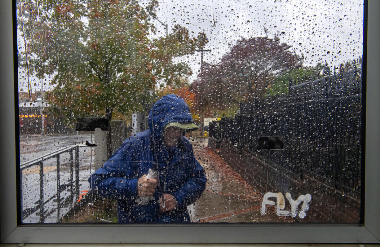 Raindrops hang on the side of a bus shelter as a passenger bundles up against the wind and rain Friday afternoon in downtown Vancouver. Stormy weather blanketed the area as an atmospheric river barreled into Washington and Oregon.