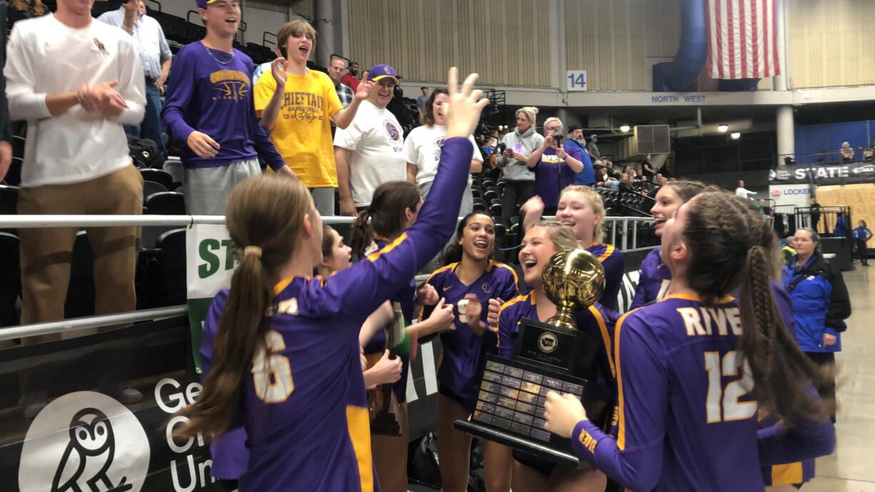Columbia River's Sofie Worden holds the state championship trophy as her teammates celebrate after the Class 2A volleyball state championship match against Ridgefield on Saturday, Nov. 19, 2022, in Yakima.