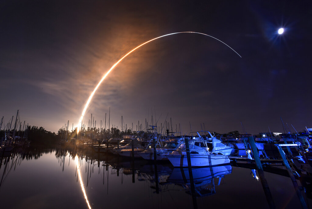 NASA's new moon rocket lifts off from the Kennedy Space Center in Cape Canaveral, Wednesday morning, Nov. 16, 2022, as seen from Harbor town Marina on Merritt Island, Fla. The moon is visible in the sky.