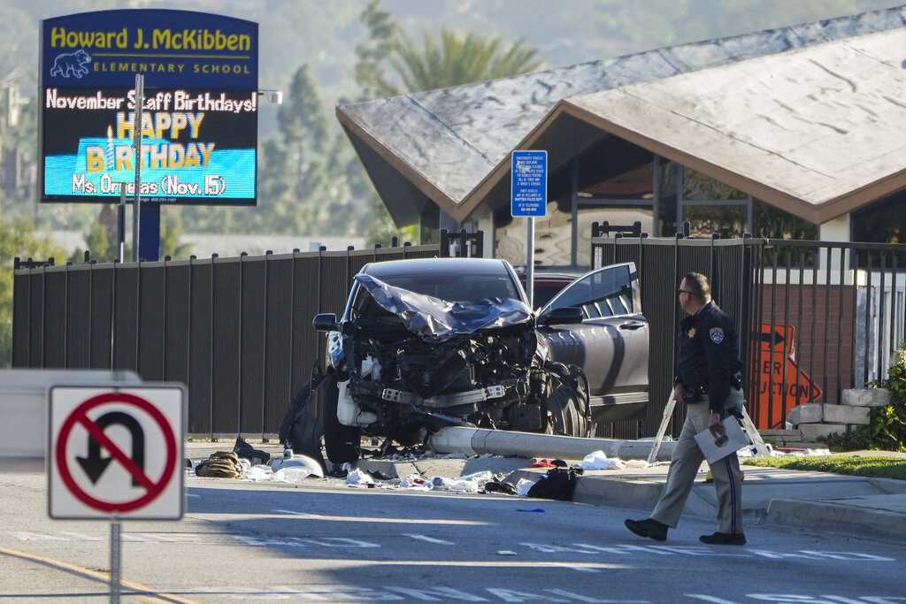 An investigator walks past a mangled SUV that struck Los Angeles County sheriff's recruits in Whittier, Calif., Wednesday, Nov. 16, 2022. The vehicle struck several Los Angeles County sheriff's recruits on a training run around dawn Wednesday, some were critically injured, authorities said. (AP Photo/Jae C.