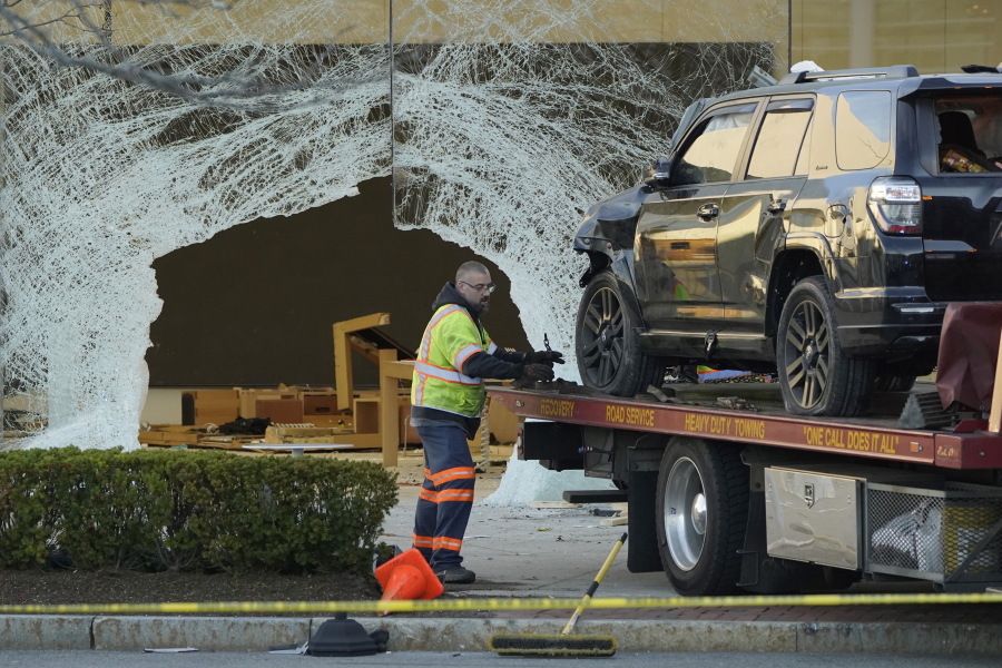 A worker secures a damaged SUV to a flatbed tow truck outside an Apple store, Monday, Nov. 21, 2022, in Hingham, Mass. At least one person was killed and multiple others were injured Monday when the SUV crashed into the store, authorities said. The crash left a large hole in the glass front of the building.