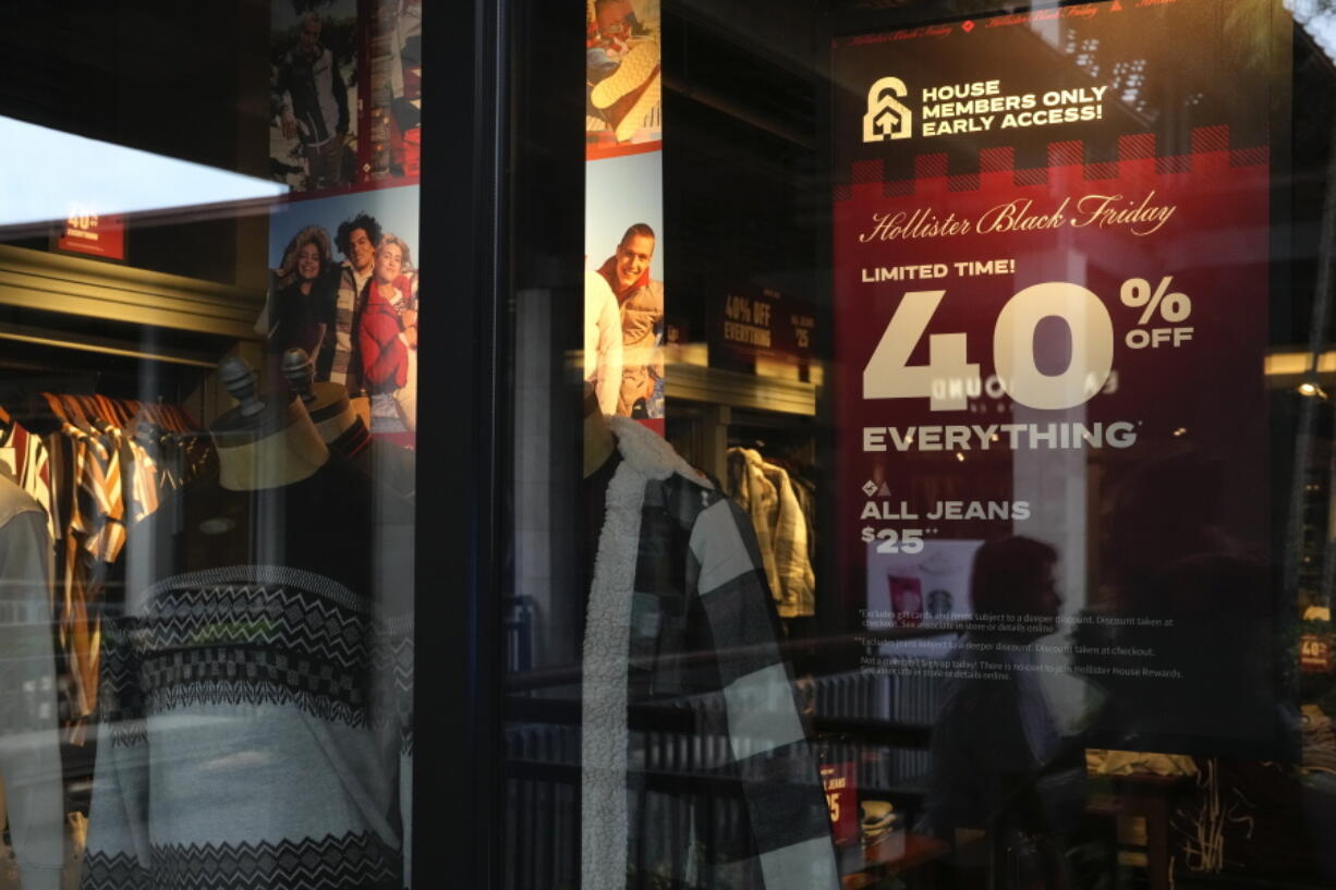 The reflections of passing shoppers are seen in the glass of a Hollister clothing store advertising sales, ahead of Black Friday and the Thanksgiving holiday, Monday, Nov. 21, 2022, in Miami. Retailers are ushering in the start of the holiday shopping season on the day after Thanksgiving, preparing for the biggest crowds since 2019.