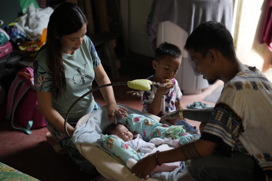 Hyancinth Charm Garing, left, and husband Jeremy, right, play with their month-old daughter inside their home at a new community for victims of super Typhoon Haiyan in Tacloban, central Philippines on Sunday Oct. 23, 2022. Garing and his family settled at a relocation site three years ago after their village was wiped out when the super typhoon struck in 2013, killing six family members and his year-old daughter.