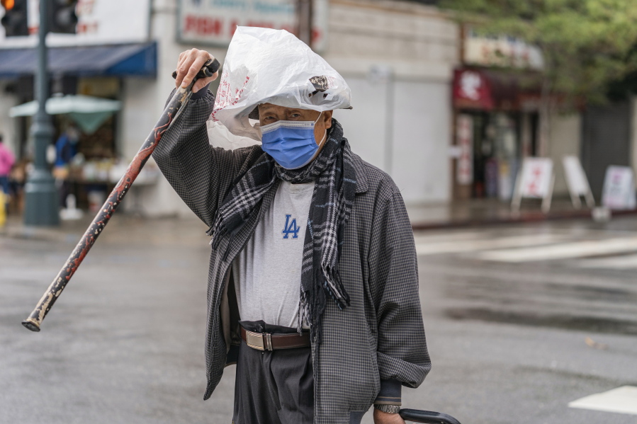 A pedestrian protects his hat from the rain with a plastic bag in the Chinatown district of Los Angeles, Monday, Nov. 7, 2022. A new Pacific storm is bringing snow, rain and wind to California. It's the second significant storm this month for the state, which remains deep in drought.