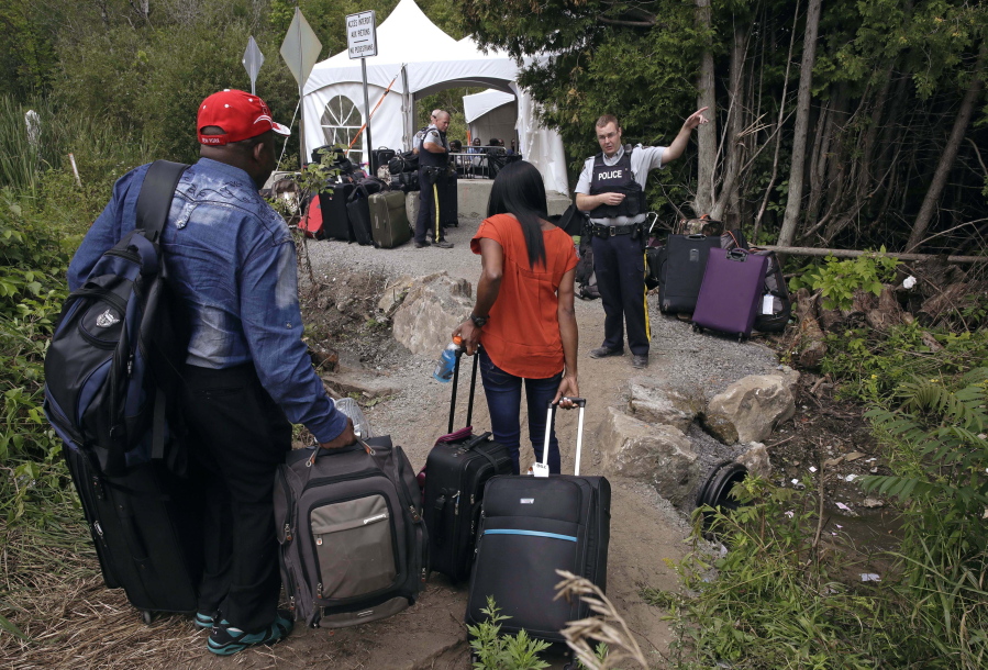 FILE - In this Aug. 7, 2017 file photo, a Royal Canadian Mounted Police officer informs a migrant couple of the location of a legal border station, shortly before they illegally crossed from Champlain, N.Y., to Saint-Bernard-de-Lacolle, Quebec, using Roxham Road. In the first nine months of 2022, the Immigration and Refugee Board of Canada finalized more than 2,700 claims by Mexican asylum seekers. Of those, 1,032 were accepted, 1,256 were rejected; and the remaining 400-plus were either abandoned, withdrawn, or had other outcomes, said Christian Tessier, an IRB spokesperson.