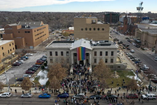 In this aerial image taken with a drone, a rainbow flag is unfurled at City Hall Wednesday, Nov. 23, 2022, in Colorado Springs, Colo. With a growing and diversifying population, the city nestled at the foothills of the Rockies is a patchwork of disparate social and cultural fabrics.