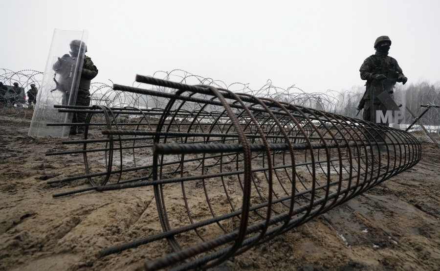 FILE - Guards and the military watching the start of work on the first part of a 180 kilometers (115 miles) and 5.5 meter (18ft)-high metal wall intended to block migrants from Belarus crossing illegally into EU territory, in Tolcze, near Kuznica, Poland, Jan. 27, 2022. When relations with Belarus deteriorated after its authoritarian President Alexander Lukashenko was declared the winner of an election widely seen as fraudulent, the government in Minsk sent thousands of migrants streaming across the EU's frontiers. In response, Poland and Lithuania erected walls along their borders with Belarus.
